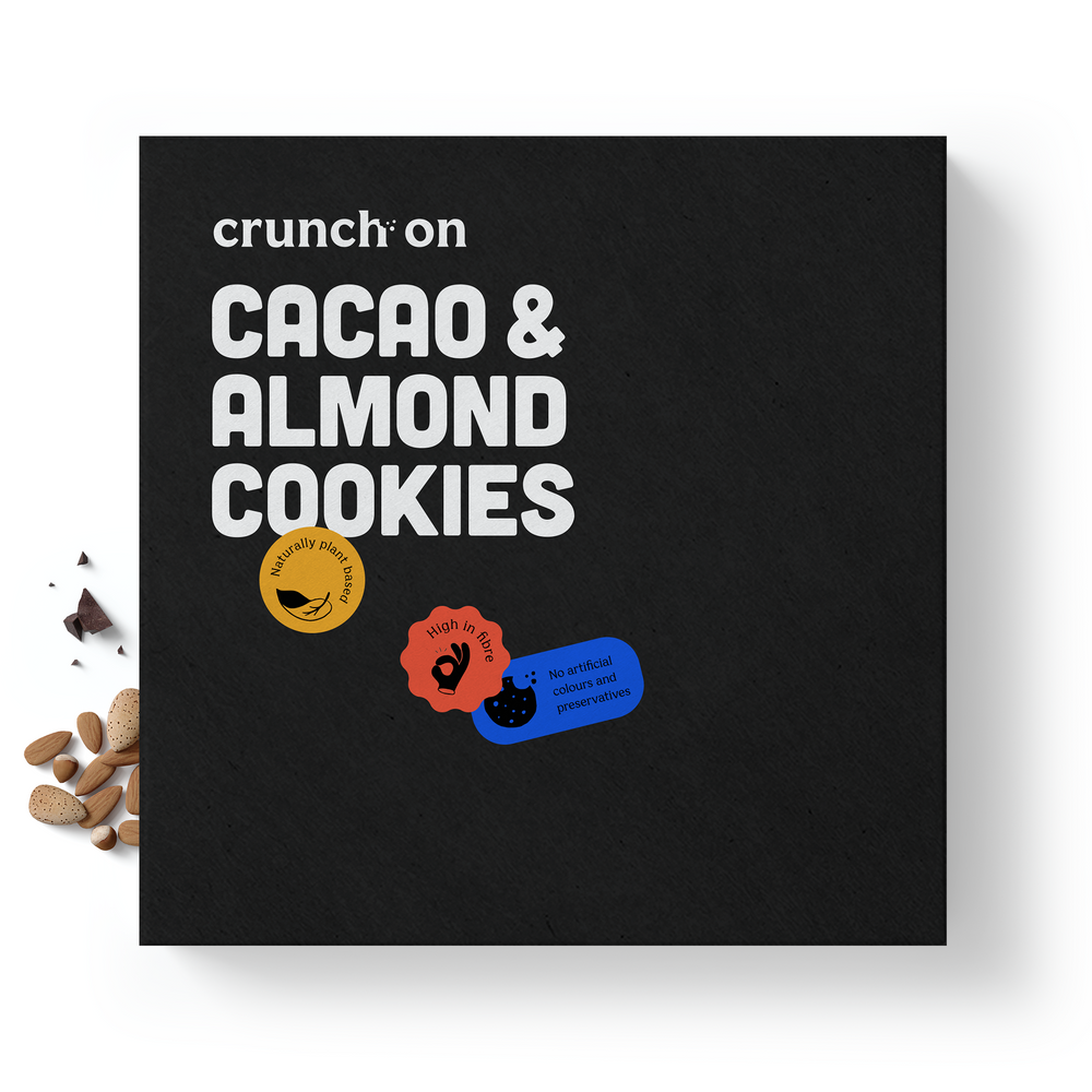 Front view of box of Crunch On Cacao & Almond Cookies, with chocolate and almonds in the background