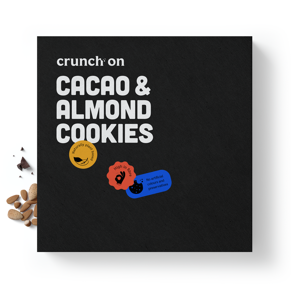 Front view of box of Crunch On Cacao & Almond Cookies - 24 cookies, with chocolate and nuts in the background